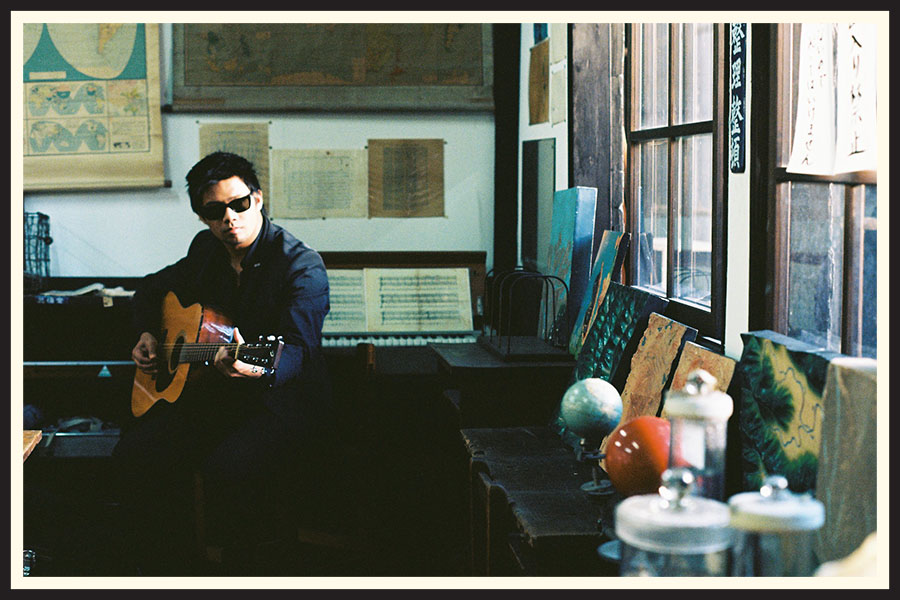 Film photo of a man in sunglasses playing an acoustic guitar captured on Kodak Ektar film.