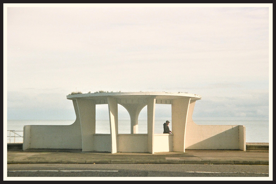 A man framed by a white structure on the side of the ocean, taken on Kodak Colorplus 200.