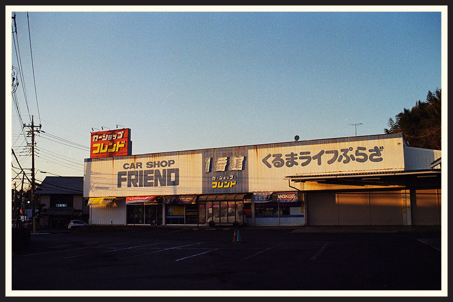 The sun sets on a storefront that reads "Car Shop Friend", taken on Kodak Colorplus 200 35mm film.